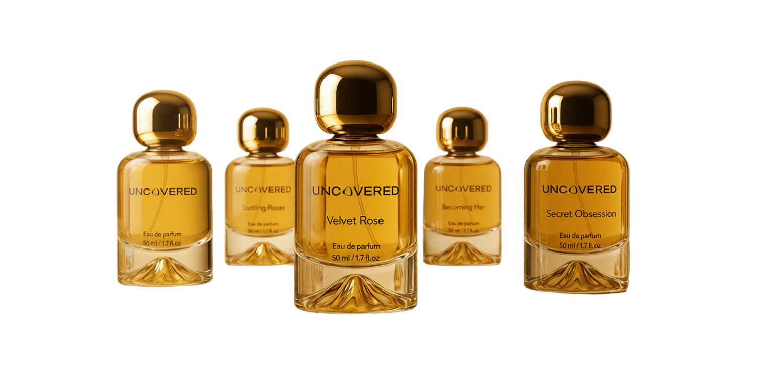 Set of five gold perfume bottles with 'UNCOVERED' branding on a reflective surface with a blurred background.