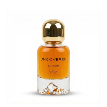 Perfume bottle labeled 'Uncovered Dark Habit' with a gold cap on a white background